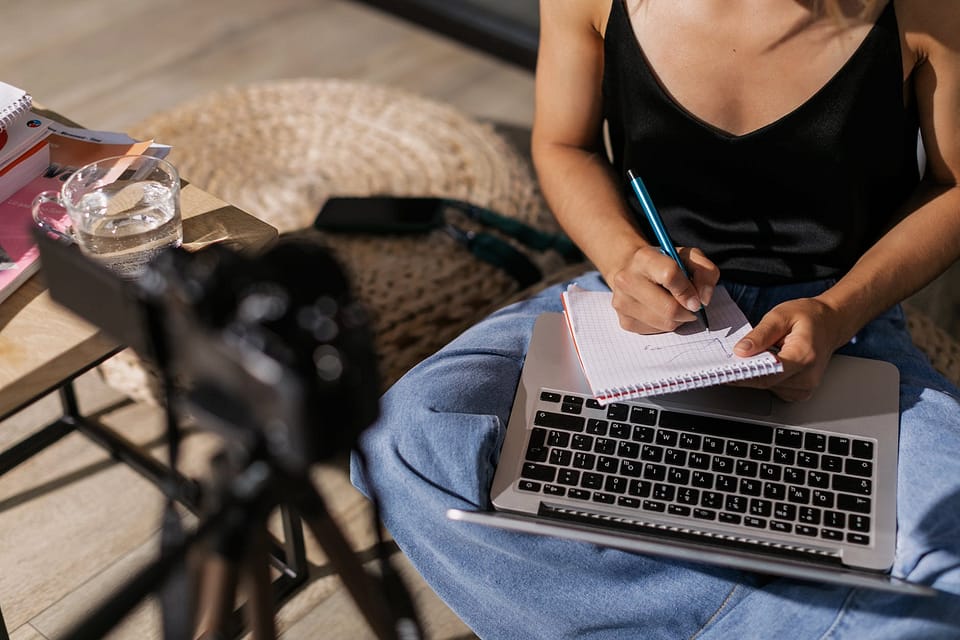 woman sitting with a laptop on her lap and writing in a notebook